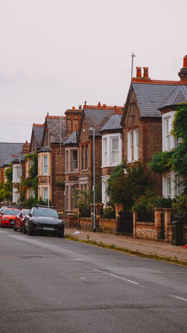 A quiet residential street in South Hornchurch featuring terraced houses with brick facades, small front gardens, and chimneys. Parked cars line both sides of the narrow asphalt road, including a whit