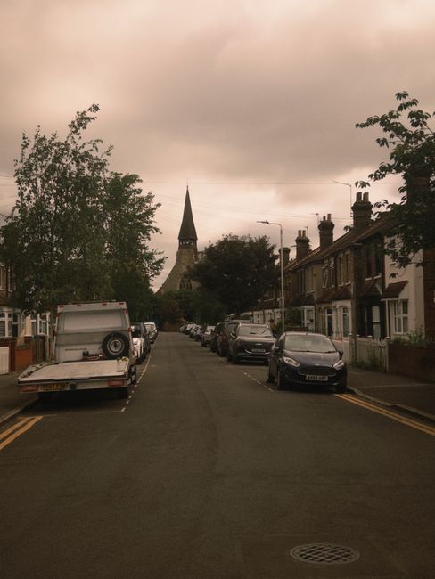 A narrow residential street in Hornchurch with closely spaced terraced houses on both sides, parked cars lining the curb, including a small flatbed vehicle with open sides positioned on the left side